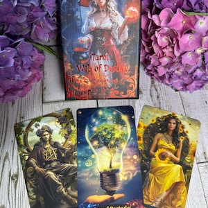 Może przedstawiać: Talia kart tarota zatytułowana "Tarot Web of Destiny" z trzema kartami. Pudełko talii przedstawia kobietę w kapeluszu czarownicy. Karty przedstawiają ilustracje kr&oacute;la, żar&oacute;wki z drzewem i kobiety w ż&oacute;łtej sukni.