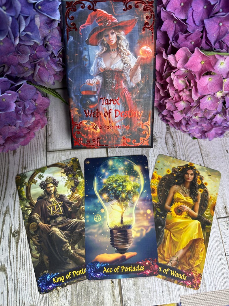Może przedstawiać: Talia kart tarota zatytułowana "Tarot Web of Destiny" z trzema kartami. Pudełko talii przedstawia kobietę w kapeluszu czarownicy. Karty przedstawiają ilustracje kr&oacute;la, żar&oacute;wki z drzewem i kobiety w ż&oacute;łtej sukni.