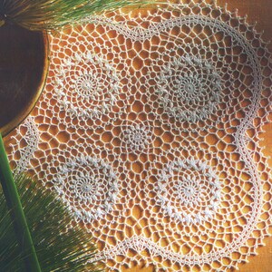 May include: White crocheted doily with a circular design featuring four smaller circles in the center.