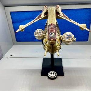 May include: A white and brown Star Wars V-4X-D starfighter model with clear plastic cockpit canopies. The model is on a black display stand with a Star Wars logo.