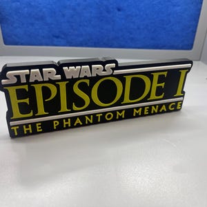 May include: A black and yellow plastic sign with the text "Star Wars Episode I The Phantom Menace".