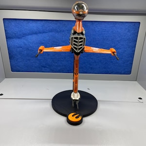 May include: An orange and gray X-wing starfighter model on a black display stand with a Rebel Alliance symbol. The model is posed in flight with the wings spread.