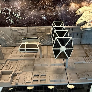 May include: A detailed diorama featuring iconic Star Wars vehicles and scenes. Includes a Millennium Falcon, TIE fighters, and an X-wing fighter, set against a backdrop of space. The model is primarily gray with black and white accents, showcasing intricate details.