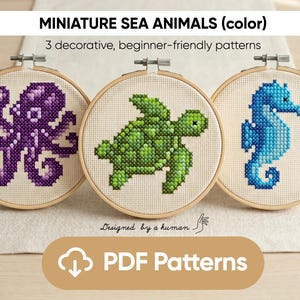 May include: Three cross-stitch patterns of sea creatures in wooden embroidery hoops. The designs include an octopus, a turtle, and a seahorse. The octopus is purple, the turtle is green, and the seahorse is blue. The text "MINIATURE SEA ANIMALS (color)" is at the top.