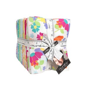 Könnte beinhalten: Ein Stapel gefalteter Stoffquadrate mit weißem Hintergrund und bunten Blumenmustern in Pink, Orange, Gelb und Türkis. Der Stapel ist mit einem weißen Band, das mit einem Linealdesign bedruckt ist, und einem Etikett mit moda fabrics supplies versehen.