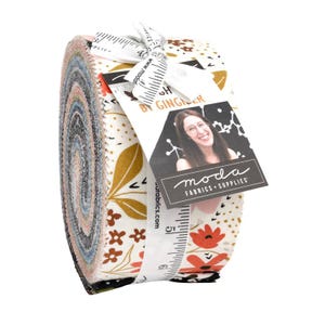 May include: A rolled fabric bundle with floral and geometric patterns in white, gold, red, and black. The bundle is tied with a ribbon and a tag that reads "MODA FABRICS + SUPPLIES" and "BY GINGER".