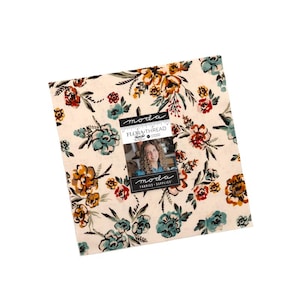 May include: A square stack of fabric squares featuring a cream background with a floral pattern in shades of teal, orange, and dark brown. A central label reads "moda FLORA THREAD" and includes a small photograph of a person with curly hair.