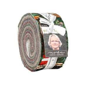 May include: A jelly roll of fabric strips featuring a variety of patterns in shades of green, red, and cream. The roll is secured with a white ribbon and a tag displaying the text Moda Fabrics + Supplies and a portrait of a person with glasses.