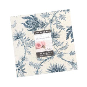 May include: A square stack of fabric squares featuring a cream background with a dark blue floral and vine pattern. A paper label is attached to the centre with the text moda, Breathtaking Blues, 3 Sisters, and moda FABRICS + SUPPLIES.