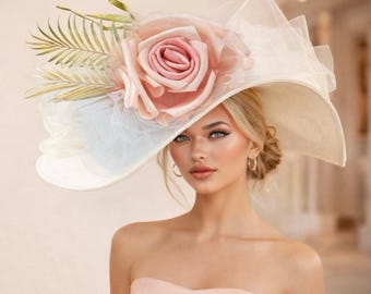 Può includere: Un cappello color crema a tesa larga ornato da una grande rosa rosa, fogliame e tessuto bianco trasparente. Il cappello è un accessorio di grande effetto, ideale per occasioni speciali. L'immagine include il testo "AIMEE FULLER".