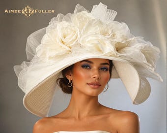 Op de afbeelding: Een ivoorkleurige hoed met brede rand, versierd met grote stoffen bloemen en transparante accenten. De hoed heeft de tekst "AIMEE FULLER" in de linkerbovenhoek. Een elegante accessoire voor bruiloften en evenementen.