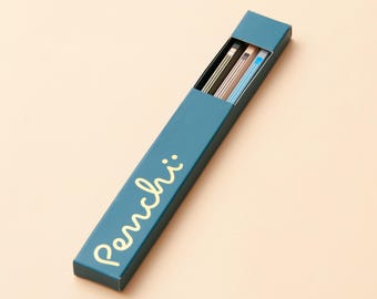 May include: A teal pencil box with the word "Penchi" in gold script. The box is open, revealing several pencils with colored stripes. The pencils are various colors, including black, brown, and blue. The background is a light peach color.