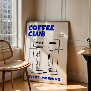 May include: A framed poster with the words "COFFEE CLUB" in blue, and the text "SERVED DAILY EVERY MORNING". The poster features a black and white illustration of a coffee machine and two people.