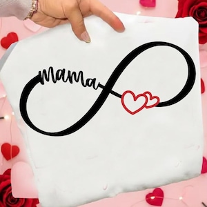 Könnte beinhalten: Weißer Stoff mit einem schwarzen Unendlichkeitszeichen-Design. Das Wort "Mama" ist in einer Schriftart innerhalb des Unendlichkeitszeichens geschrieben. Zwei rote Herzen befinden sich auf der rechten Seite des Symbols. Der Stoff wird von einer Hand gehalten.