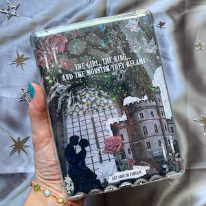 May include: A clear phone case with a fantasy theme. The case features a castle, roses, and the text "THE GIRL, THE KING... AND THE MONSTER THEY BECAME" and "GET LOST IN FANTASY". The design includes a silhouette of a couple kissing.