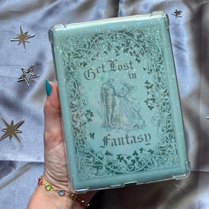 May include: A light blue case with the words "Get Lost in Fantasy" and an illustration of a couple. The case has a clear border and is decorated with glitter and floral designs. The case is rectangular.