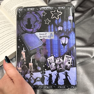 Può includere: Una custodia protettiva trasparente per tablet con un design a collage in tonalità viola e nere. La grafica include un gatto su una luna crescente, lanterne sospese, candele, boccette, carte dei tarocchi e sagome con il testo Season of the Witch.