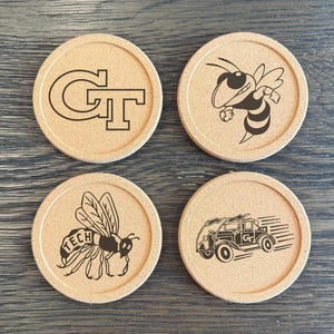 May include: Four circular coasters with a light brown cork base. Each coaster features a black graphic: the letters "GT", a cartoon bee, a bee with "TECH" on its body, and a vintage car with "GT" on the side.