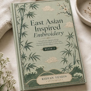 May include: A hardback book titled East Asian Inspired Embroidery Book 2 by Ridvan Yusein. The sage green cover features illustrations of bamboo, clouds, waves, and floral sprigs. The text includes Lotus Flowers, Bamboo Sprigs, Chrysanthemum Motifs, Crane Forms, Wave Borders and Elegant Textile Panels.