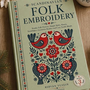 May include: A hardback book titled Scandinavian Folk Embroidery by Ridvan Yusein, Book 3. The sage green cover features dark blue and red illustrations of birds, flowers, hearts, and snowflakes, with a vertical border of small red hearts.