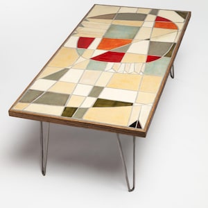 May include: A rectangular coffee table with a geometric tile top in shades of beige, green, red, and blue. The table has four hairpin legs.