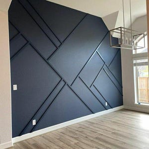 May include: A modern interior featuring a navy blue accent wall with geometric paneling. The wall is contrasted by a white ceiling and trim, and a light wood-look floor. A rectangular light fixture hangs from the ceiling.
