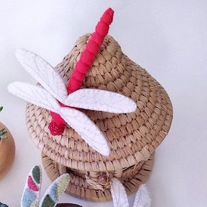 Op de afbeelding: Drie vilt libellen ornamenten in verschillende kleuren en patronen. Eén libel is rood en wit, één is groen en wit met kleurrijke accenten en één is wit met een groen lichaam.