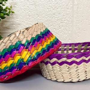 May include: Two woven baskets, one with a rainbow colored trim and the other with a purple trim.