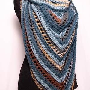 May include: A crocheted shawl in shades of blue, brown, and beige. The shawl is triangular in shape and has a lacy pattern.
