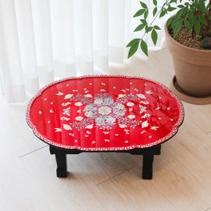 May include: A red oval table with a floral design and black legs. The table top is decorated with a floral pattern and butterflies.