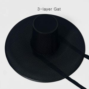 K&ouml;nnte beinhalten: Ein schwarzer, dreilagiger Gat-Hut mit breiter Krempe und zylindrischer Krone. Der Hut hat ein strukturiertes, gepunktetes Muster und schwarze Riemen. Der Text "3-layer Gat" ist oben im Bild zu sehen.