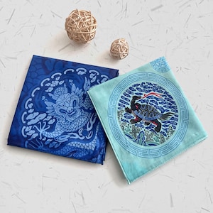Peut inclure: Deux carrés de tissu décoratifs. L'un est bleu foncé avec un motif de dragon bleu clair. L'autre est bleu clair avec un motif de tortue dans un cadre circulaire. Deux petites sphères tissées sont en arrière-plan.