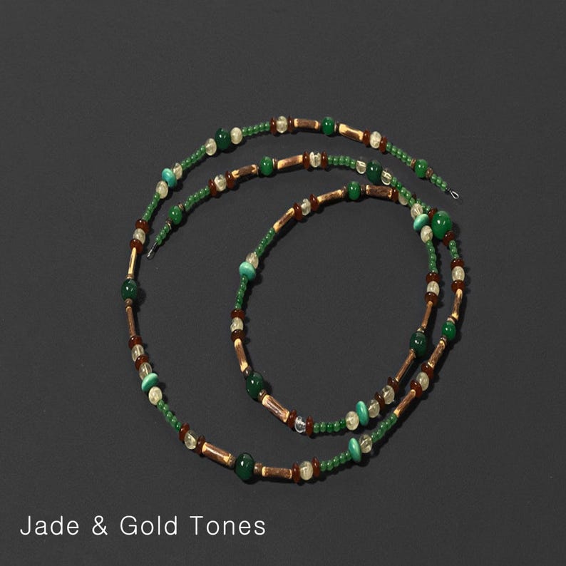 K&ouml;nnte beinhalten: Eine Halskette in Jade- und Goldt&ouml;nen. Die Halskette hat eine Kombination aus gr&uuml;nen, goldenen und braunen Perlen. Die Perlen sind zu einem langen, eleganten Design aufgereiht. Der Text "Jade & Gold Tones" steht unten.