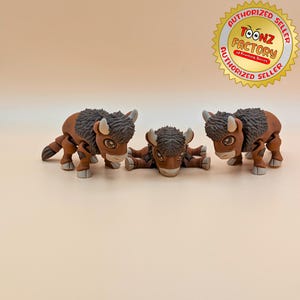 May include: Three brown bison figurines with black fur and white hooves. The bison are in different poses, one standing, one lying down, and one standing with its head turned to the side.