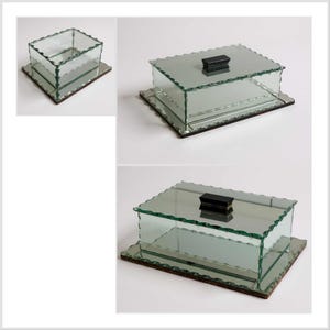 May include: A rectangular glass box with a mirrored base and a black rectangular knob on the lid. The edges of the glass are scalloped. The box is displayed on a white background.