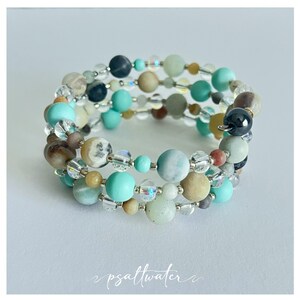 May include: A multi-strand bracelet featuring a variety of colorful beads in shades of turquoise, beige, gray, and clear crystal. The bracelet is made with elastic cord and has a wrap-around design. The beads vary in size and texture, creating a unique and eye-catching accessory.