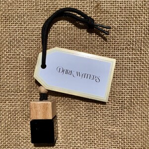 Peut inclure: Un d&eacute;sodorisant avec une &eacute;tiquette indiquant "Dark Waters". Le d&eacute;sodorisant a un cordon noir et un design de cube en bois et noir. L'&eacute;tiquette est blanche avec une bordure dor&eacute;e. Le fond est une texture de toile de jute.