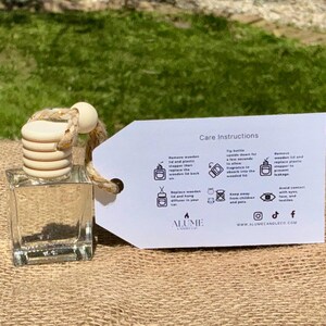 Peut inclure: Un flacon diffuseur carr&eacute; en verre transparent avec un couvercle en bois et une corde beige. Une &eacute;tiquette blanche avec des instructions d'entretien est attach&eacute;e. Le flacon est pos&eacute; sur une surface en toile de jute avec un fond herbeux vert.