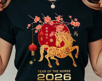 May include: Black t-shirt featuring a gold horse design with floral accents, a red circle, and a hanging lantern. The text "Year of the Horse 2026" is displayed in gold. The design celebrates the Chinese New Year.