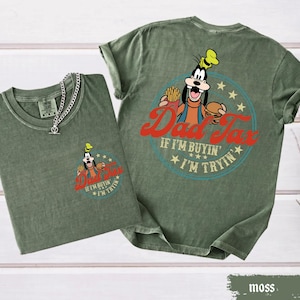 May include: Two moss green t-shirts with a graphic of a cartoon character holding a burger and fries, with the text "Dad Tax" and "If I'm buyin', I'm tryin'". One shirt has a silver chain necklace.