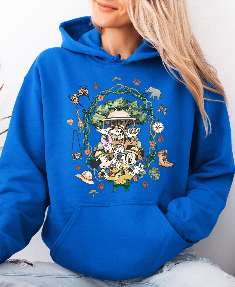 Peut inclure: Sweat &agrave; capuche bleu roi avec un motif sur le th&egrave;me du safari. Le design comprend Mickey Mouse, Donald Duck, Dingo et d'autres personnages en tenue de safari, entour&eacute;s d'ic&ocirc;nes li&eacute;es au safari comme une boussole, des jumelles et un appareil photo. Le motif est centr&eacute; sur le devant.