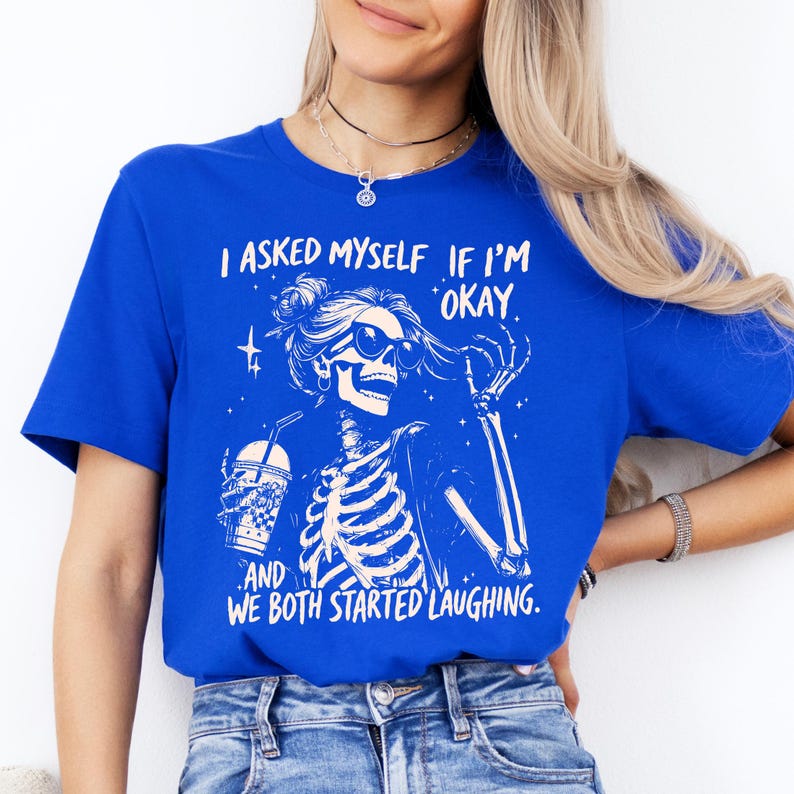 May include: Royal blue t-shirt featuring a white graphic of a skeleton wearing sunglasses and holding a drink. The text on the shirt reads, "I asked myself if I'm okay, and we both started laughing."