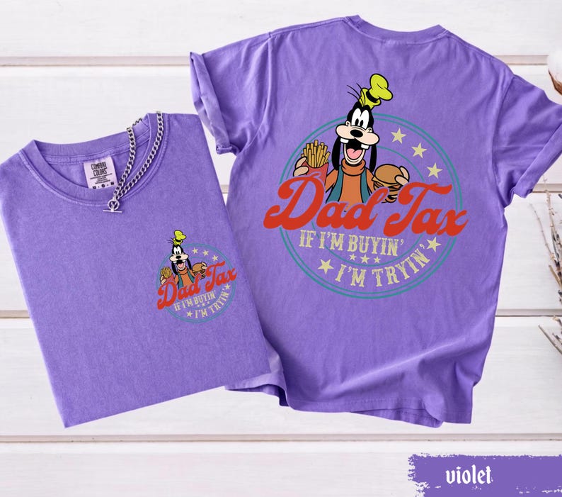 May include: Two violet-colored t-shirts. One shirt has a small graphic of Goofy with the words "Dad Tax" and "If I'm buyin' I'm tryin'". The other shirt has the same graphic on the back. A silver chain necklace is on the front of one shirt.