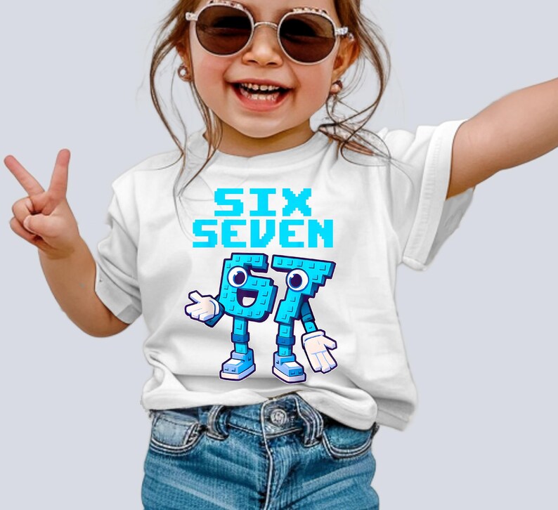 May include: White t-shirt with the words "SIX SEVEN" in pixelated blue letters. Below the text are the numbers 6 and 7 designed as cartoon characters in blue with white gloves and shoes. The shirt is worn by a child.