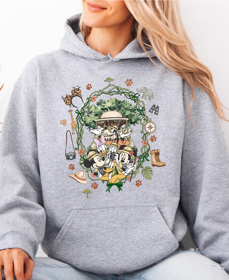 Peut inclure: Un sweat &agrave; capuche gris clair avec un motif color&eacute; de personnages de dessins anim&eacute;s en tenue de safari. Le motif comprend un arbre, des animaux et des accessoires sur le th&egrave;me du safari. Le sweat &agrave; capuche a une poche kangourou et une capuche &agrave; cordon.