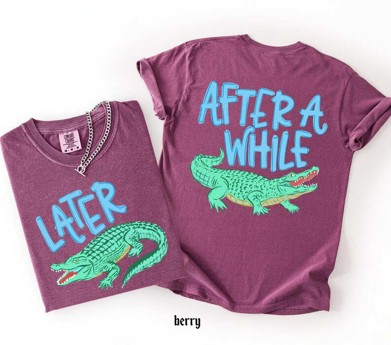 May include: Two berry-colored t-shirts with the text "LATER" and "AFTER A WHILE" in light blue. Each shirt features a green alligator graphic. A silver chain necklace is on one shirt.