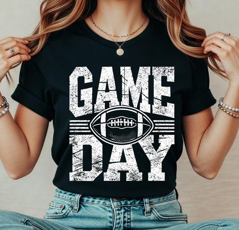 Puede incluir: Camiseta negra con la frase "GAME DAY" en letras blancas desgastadas. Un gr&aacute;fico de f&uacute;tbol americano blanco est&aacute; centrado entre las palabras. La camiseta es de estilo casual.