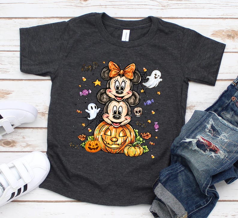 Puede incluir: Camiseta gris oscuro con un dise&ntilde;o de Halloween. El dise&ntilde;o presenta a los personajes de Mickey y Minnie Mouse apilados sobre una calabaza tallada, rodeados de fantasmas, murci&eacute;lagos y caramelos. La camiseta se muestra con vaqueros azules y zapatillas blancas.