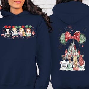 May include: Navy blue hooded sweatshirt featuring a colorful graphic of Disney princesses on the front and back. The front design shows four princesses with Mickey Mouse ears and candy canes. The back design features a castle and fireworks.