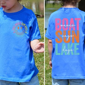 May include: A blue t-shirt featuring a smiley face and the words "Sun Rays & Sunny Days" on the front. The back of the shirt displays the words "Boat Waves Sun Rays Lake Days" in different colours.